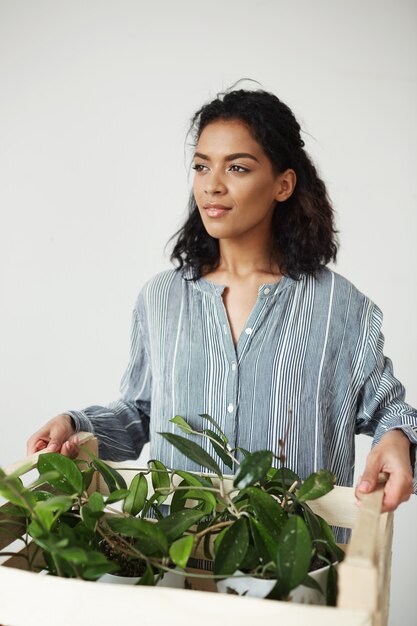 Hermosa mujer botánico sonriente sosteniendo caja con plantas