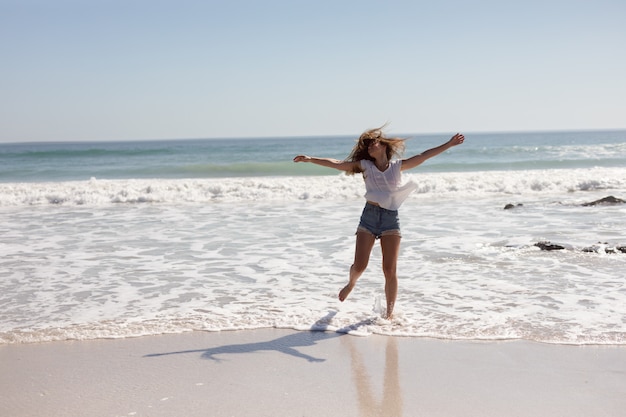 Hermosa mujer con los brazos estirados caminando en la playa bajo el sol