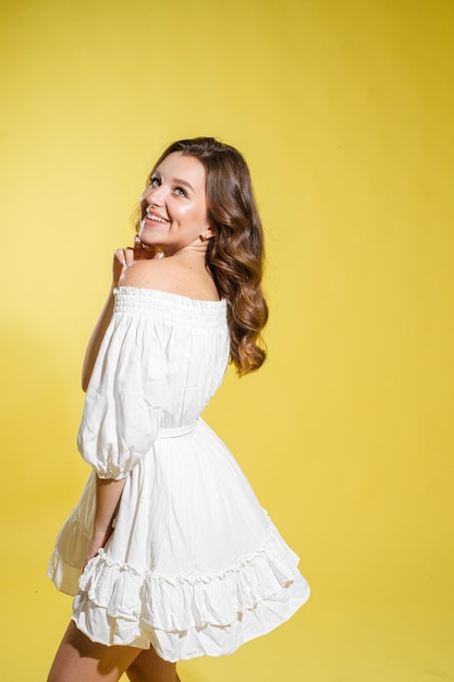 Hermosa mujer brillante en el estudio sobre un fondo amarillo con un vestido de luz blanca sonriendo feliz