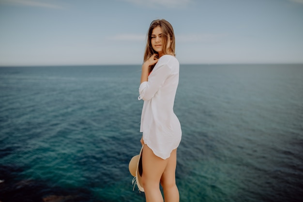 Hermosa mujer bronceada en camisa blanca mirando a la cámara en el océano