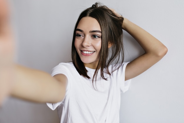 Hermosa mujer bronceada con ojos marrones haciendo selfie y riendo. dama elegante aislada.