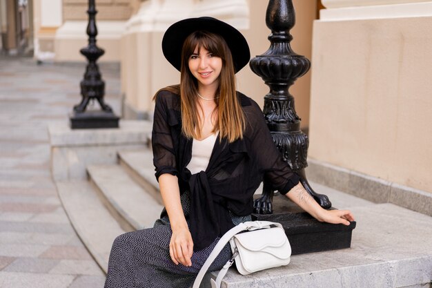 Hermosa mujer bruneete en elegante traje de otoño y sombrero de espalda posando en la calle en la vieja ciudad europea