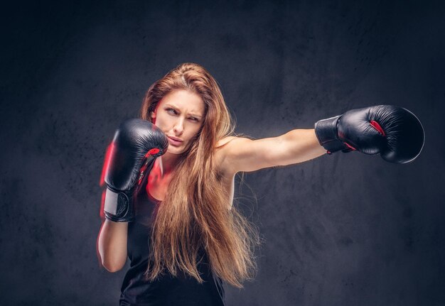 Hermosa mujer con cabello largo está demostrando su éxito en el estudio. Ella está usando guantes de boxeo.