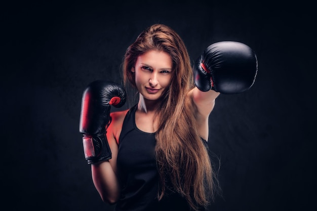 Hermosa mujer con cabello largo está demostrando su éxito en el estudio. Ella está usando guantes de boxeo.