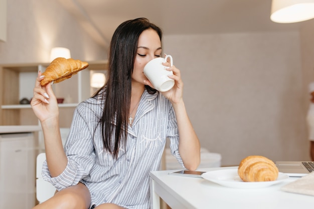 Hermosa mujer con cabello negro brillante tomando café durante el desayuno