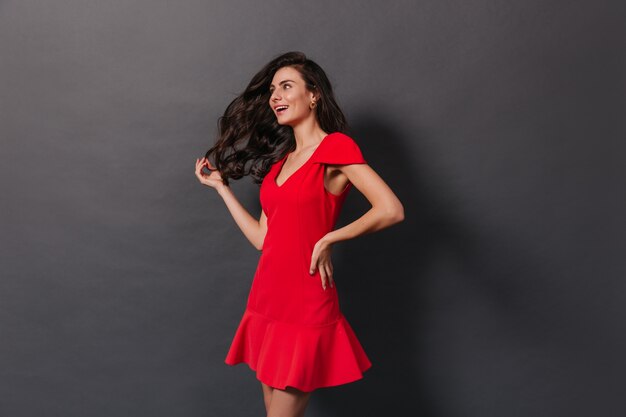 Hermosa mujer con cabello ondulado magnífico posando en traje rojo sobre fondo oscuro.