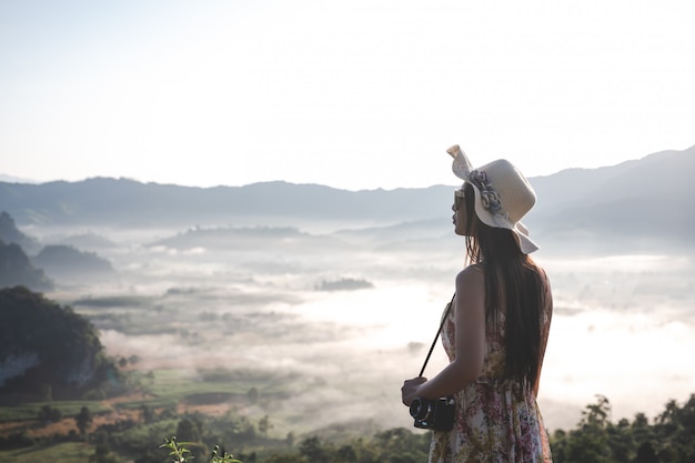 Hermosa mujer con una cámara de pie en la cima de la montaña