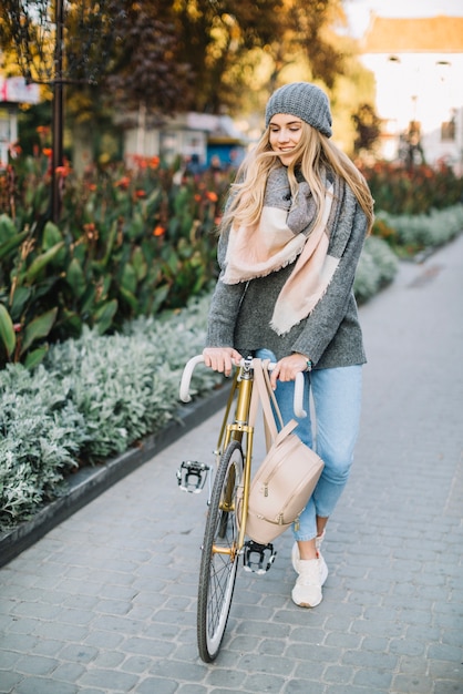 Hermosa mujer caminando con bicicleta cerca de flores