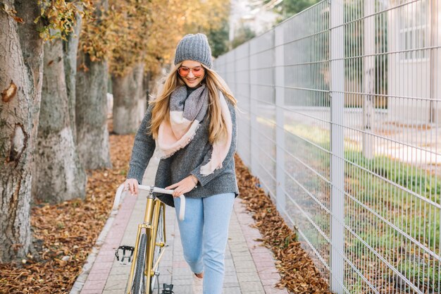 Hermosa mujer caminando con bicicleta cerca de la valla