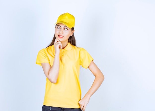 Hermosa mujer en camiseta amarilla y gorra mirando a su lado sobre fondo blanco.