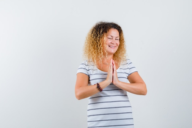 Hermosa mujer en camiseta cogidos de la mano en gesto de oración y mirando esperanzado, vista frontal.