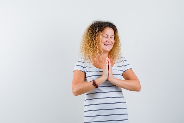 Hermosa mujer en camiseta cogidos de la mano en gesto de oración y mirando esperanzado, vista frontal.