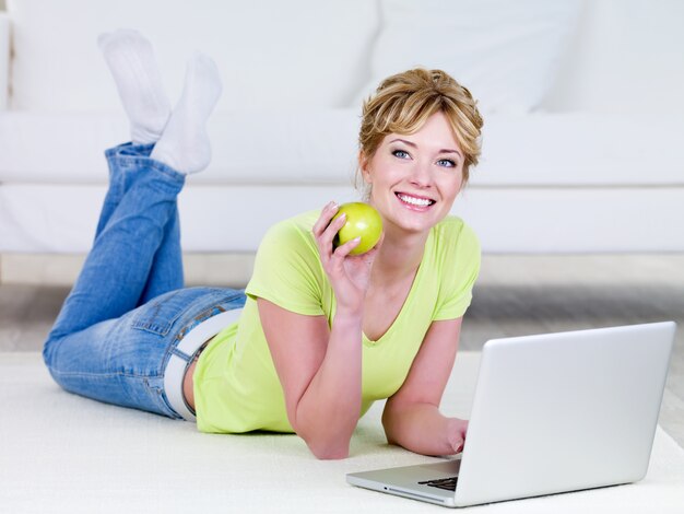 Hermosa mujer en casual con laptop comiendo manzana verde - en el interior