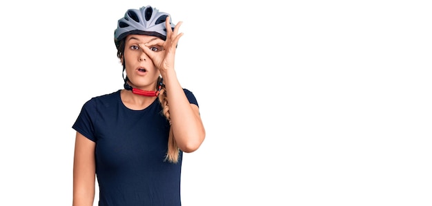 Hermosa mujer caucásica con casco de bicicleta haciendo un buen gesto sorprendida con la cara sorprendida, mirando a los ojos a través de los dedos. expresión incrédula.