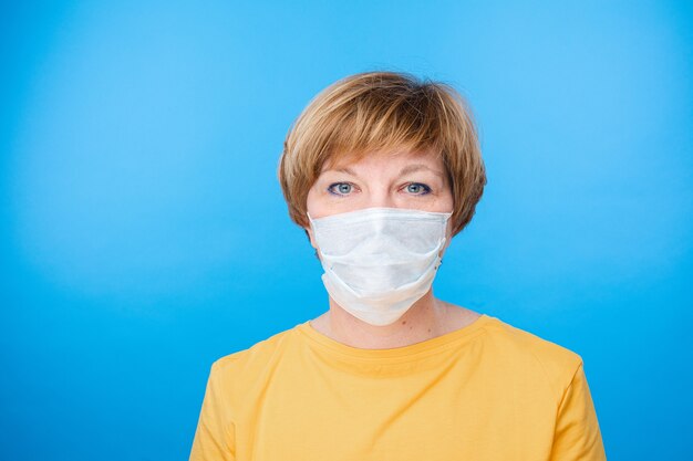 Hermosa mujer caucásica con máscara médica especial, retrato aislado sobre fondo azul.