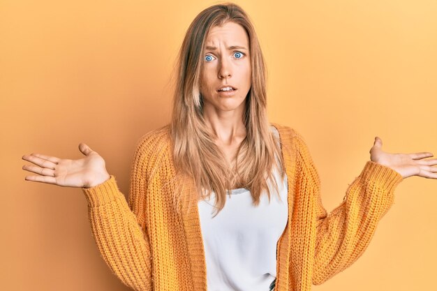 Hermosa mujer caucásica con ropa informal sin idea y confundida con los brazos abiertos sin idea y cara dudosa