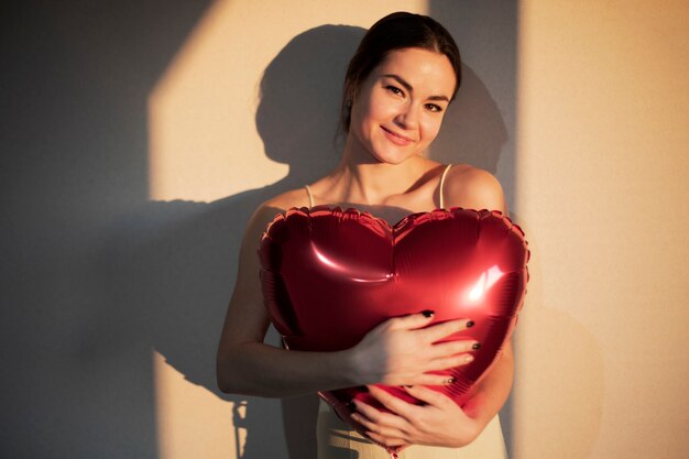 Hermosa mujer celebrando el día de San Valentín mientras sostiene un globo rojo en forma de corazón