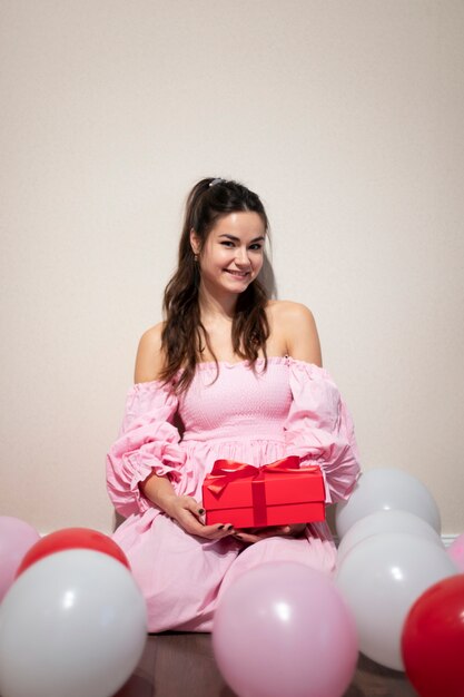 Hermosa mujer celebrando el día de San Valentín con un vestido rosa con globos y presente