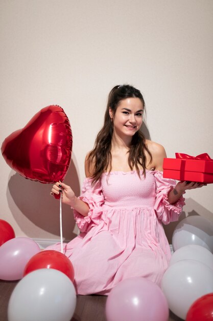 Hermosa mujer celebrando el día de San Valentín con un vestido rosa con globos y presente