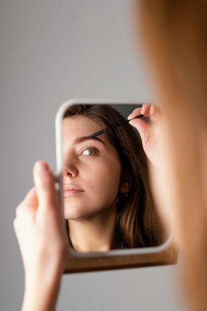 Hermosa mujer cepillándose las cejas mientras se mira en el espejo después del tratamiento