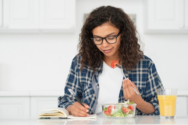 Hermosa mujer comiendo ensalada y escribiendo