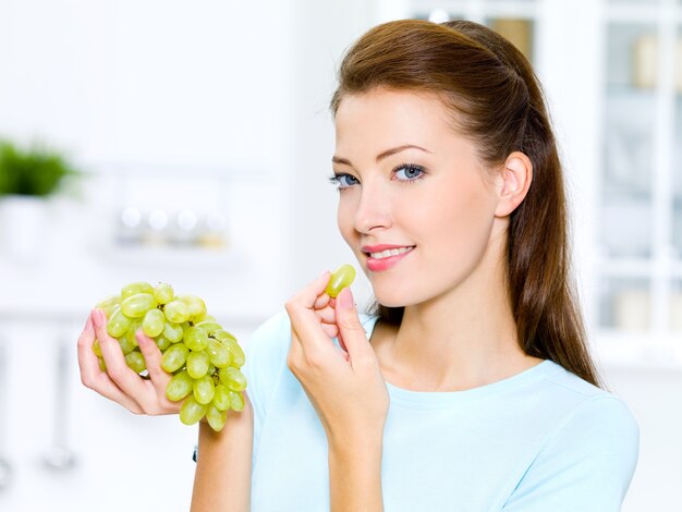 Hermosa mujer comiendo uvas está en la cocina