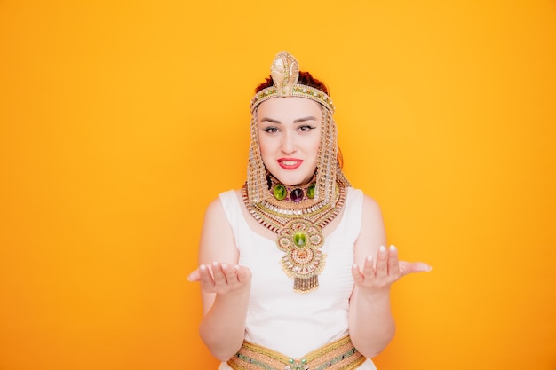 Hermosa mujer como Cleopatra en traje egipcio antiguo levantando las manos con disgusto en naranja