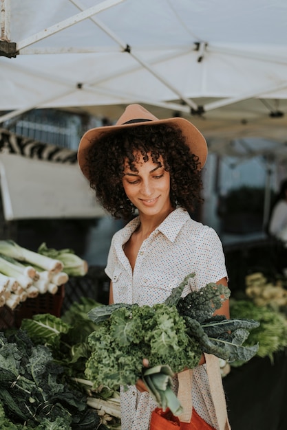 Hermosa mujer comprando col rizada en un mercado de agricultores