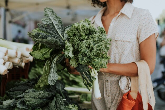 Hermosa mujer comprando col rizada en un mercado de agricultores