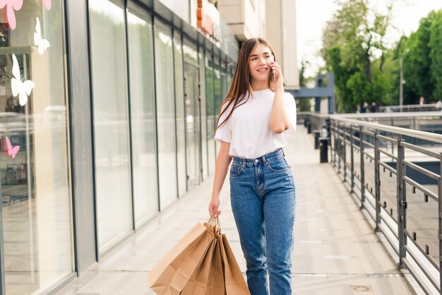 Hermosa mujer de compras hablando por su teléfono celular caminando con bolsas en la calle