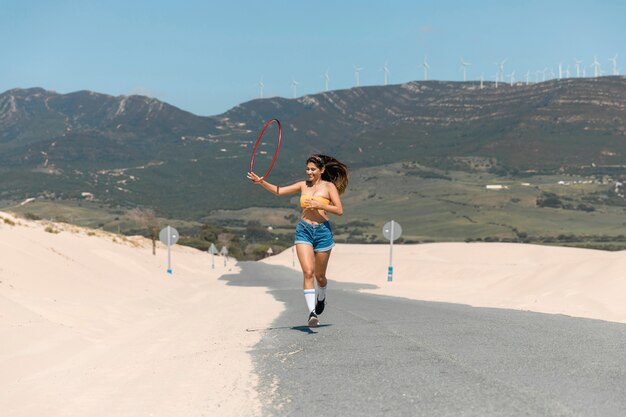 Hermosa mujer corriendo con hula hoop en la arena