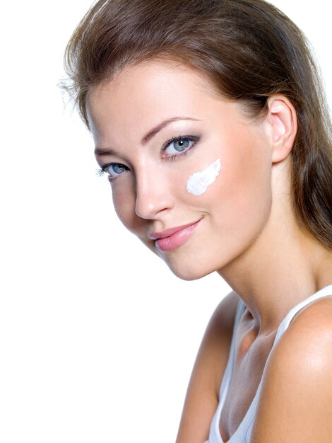 Hermosa mujer con crema cosmética humectante en la cara aislada en blanco