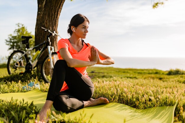 Hermosa mujer delgada haciendo deporte en la mañana en el parque haciendo yoga