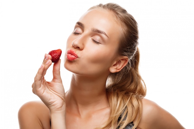 Hermosa mujer deportiva posando, comiendo fresa