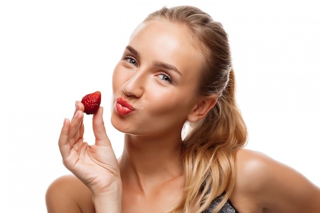 Hermosa mujer deportiva posando, comiendo fresa