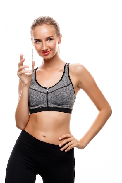 Hermosa mujer deportiva posando, sosteniendo un vaso de agua