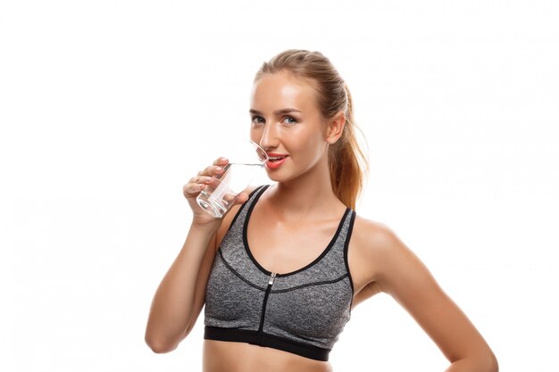 Hermosa mujer deportiva posando, sosteniendo un vaso de agua