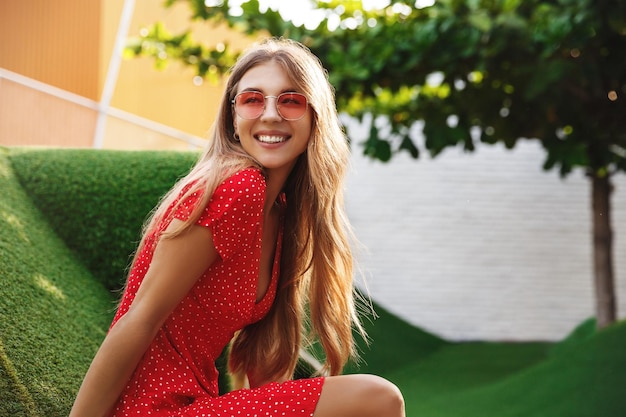 Hermosa mujer descansando sobre la hierba y sonriendo disfrutando de las vacaciones de verano tropical con gafas de sol y vestido