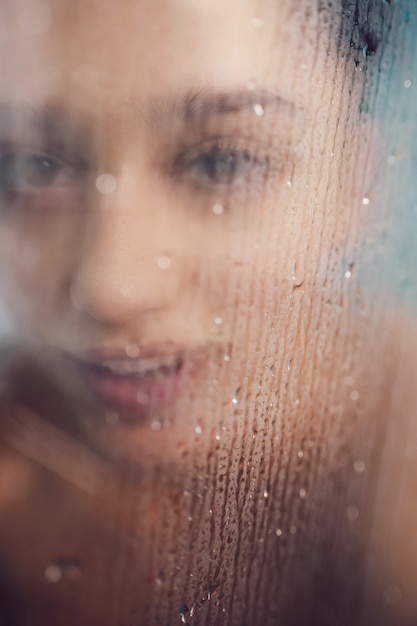 Hermosa mujer detrás del vidrio con gotas de agua.