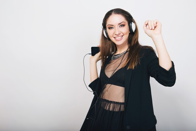 Hermosa mujer elegante aislada en traje negro escuchando música en auriculares bailando