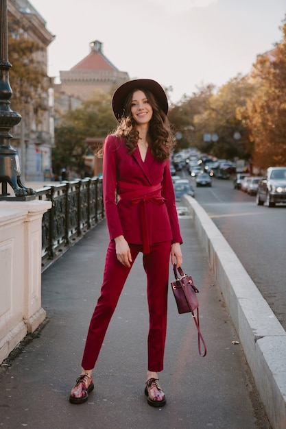 Hermosa mujer elegante hermosa en traje morado caminando en las calles de la ciudad, tendencia de moda primavera verano otoño temporada con sombrero, sosteniendo el bolso