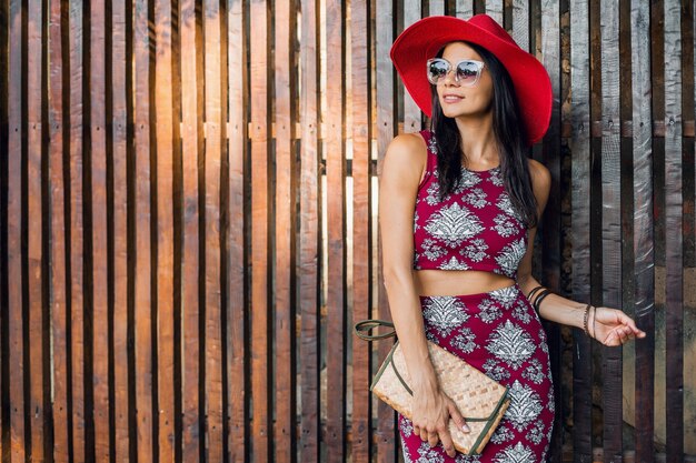 Hermosa mujer elegante posando contra la pared de madera en traje de estilo tropical