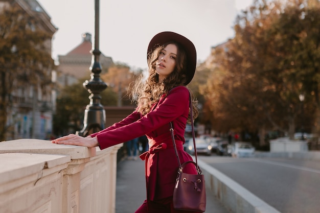Hermosa mujer elegante en traje púrpura caminando en las calles de la ciudad, tendencia de moda primavera verano otoño temporada con sombrero, sosteniendo el bolso