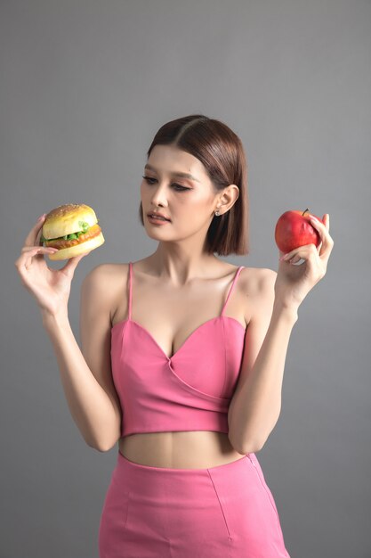 Hermosa mujer eligiendo entre manzana y hamburguesa