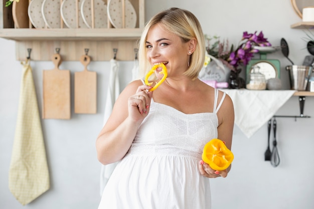 Hermosa mujer embarazada comiendo pimiento amarillo