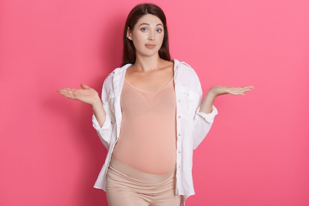 Foto gratuita hermosa mujer embarazada europea de pelo oscuro alegre en traje cómodo extendiendo las manos con expresión de asombro