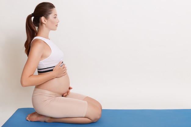 Hermosa mujer embarazada haciendo yoga en casa