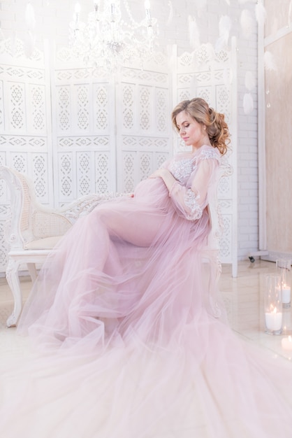 Hermosa mujer embarazada en rico vestido rosa tiene las manos en su vientre posando