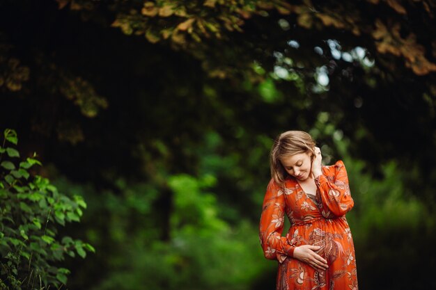 Hermosa mujer embarazada en vestido naranja plantea en el bosque