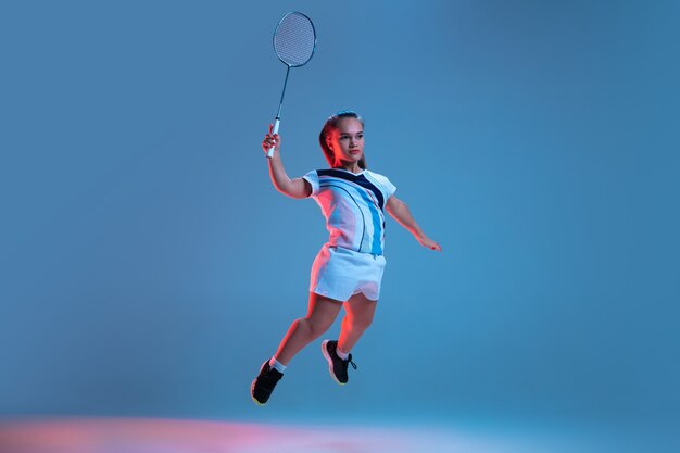 Hermosa mujer enana practicando bádminton aislado en azul en luz de neón